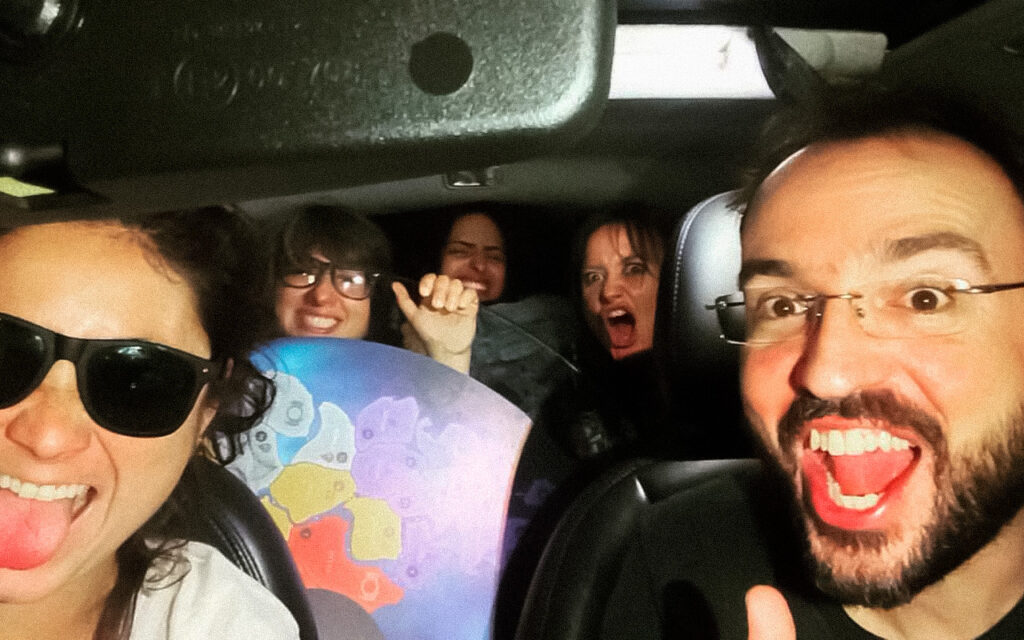 Grupo de pessoas sorrindo e fazendo caretas dentro de um carro, celebrando de forma descontraída após uma experiência criativa com o jogo, com clima de amizade, empolgação e conquista coletiva.