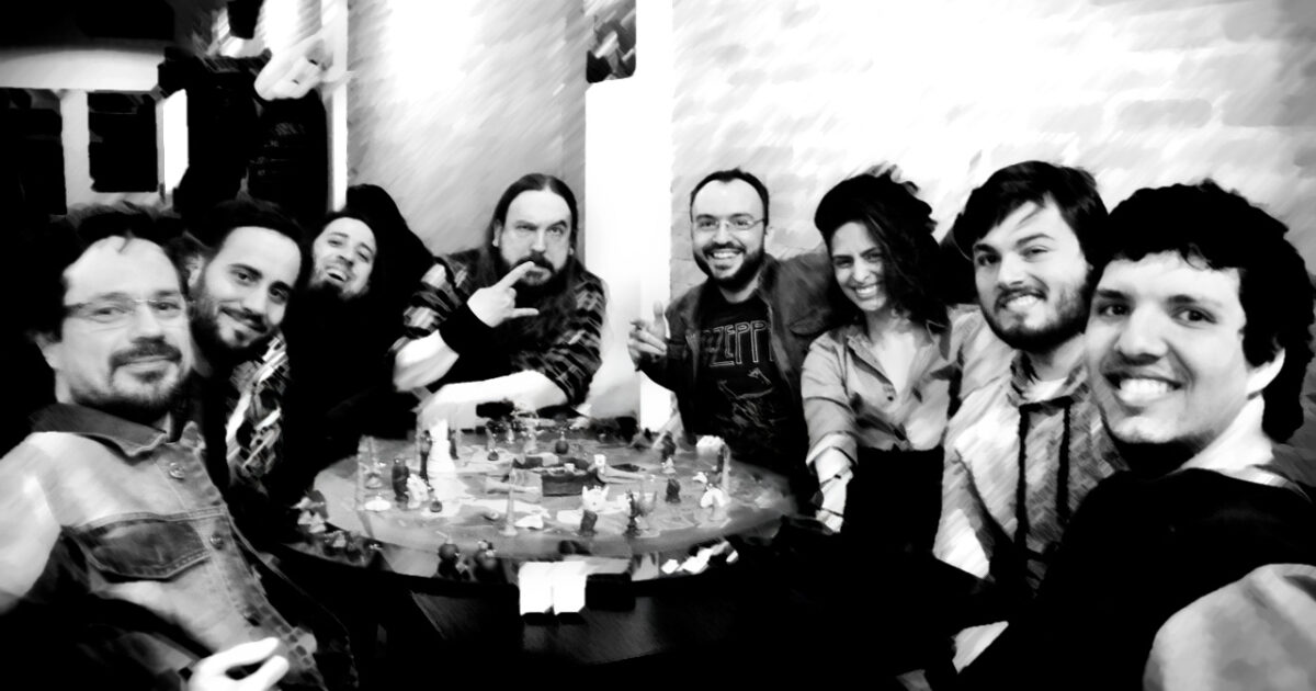 Grupo de pessoas reunidas em torno de um tabuleiro criativo, sorrindo para a câmera, cercadas por criaturas, torres e elementos artesanais do jogo.