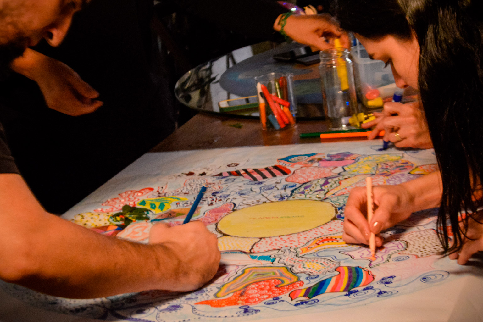 Pessoas criando juntas um mapa colorido à mão, usando lápis e canetas, em uma atividade criativa coletiva inspirada no jogo de tabuleiro criativo Planeta Insano.