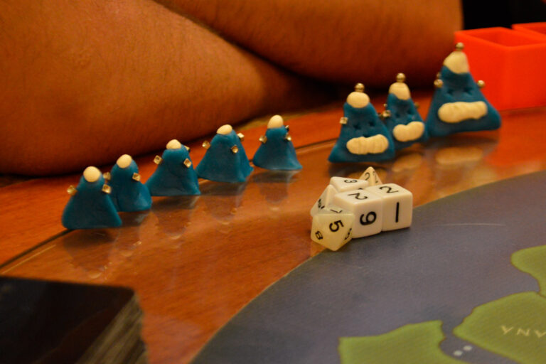 Criaturas azuis do Planeta Insano alinhadas sobre a mesa durante partida na Ludos Luderia, com dados de RPG posicionados à frente, sugerindo expectativa e tensão antes da ação.