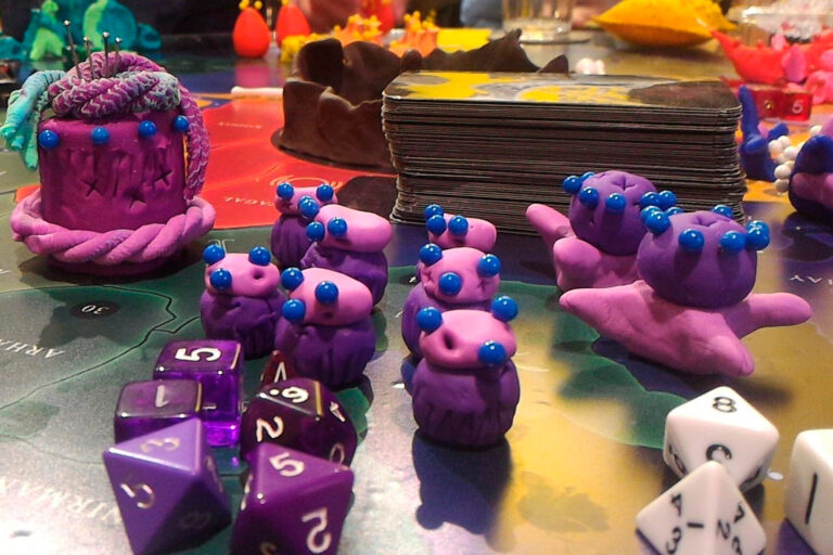 Espécies do jogo de tabuleiro Planeta Insano moldadas em massinha ao lado de dados e cartas durante uma Terça Nerd