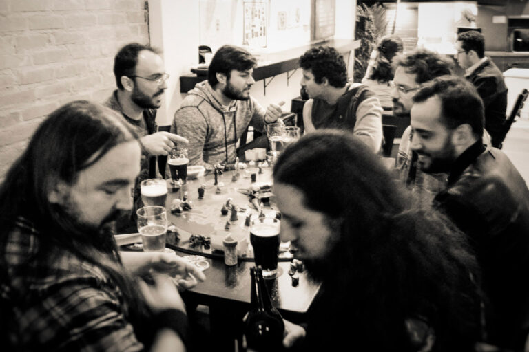 Jogadores debatendo estratégias ao redor do tabuleiro do Planeta Insano durante uma Terça Nerd