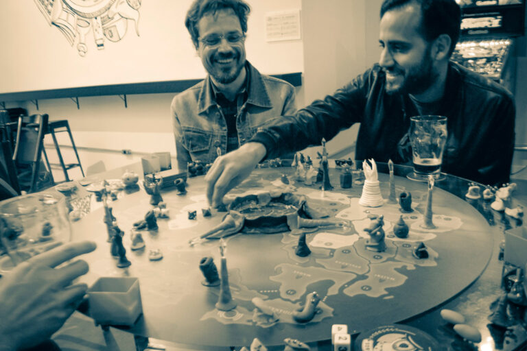 Jogadores sorrindo enquanto realizam uma jogada no tabuleiro do Planeta Insano durante uma Terça Nerd