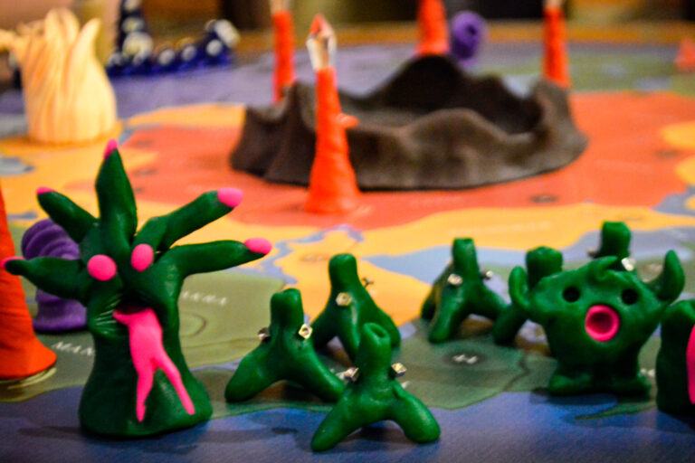 Criaturas verdes moldadas em massinha ocupando o tabuleiro do jogo Planeta Insano durante uma Terça Nerd