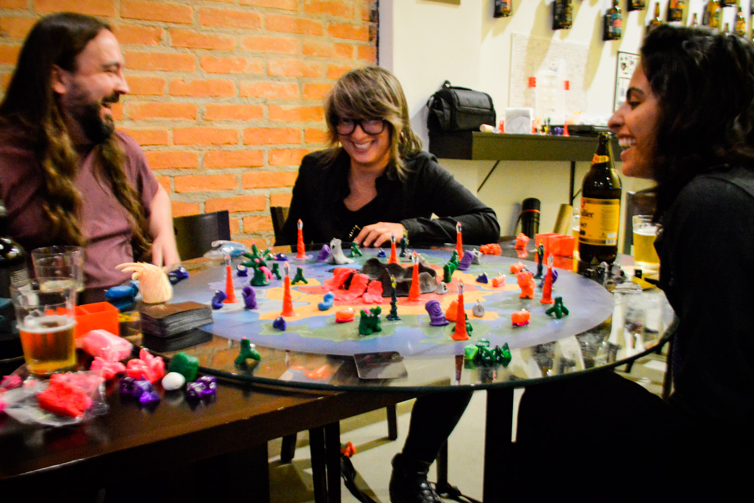 Pessoas jogando e sorrindo em volta do tabuleiro do jogo Planeta Insano durante a Terça Nerd